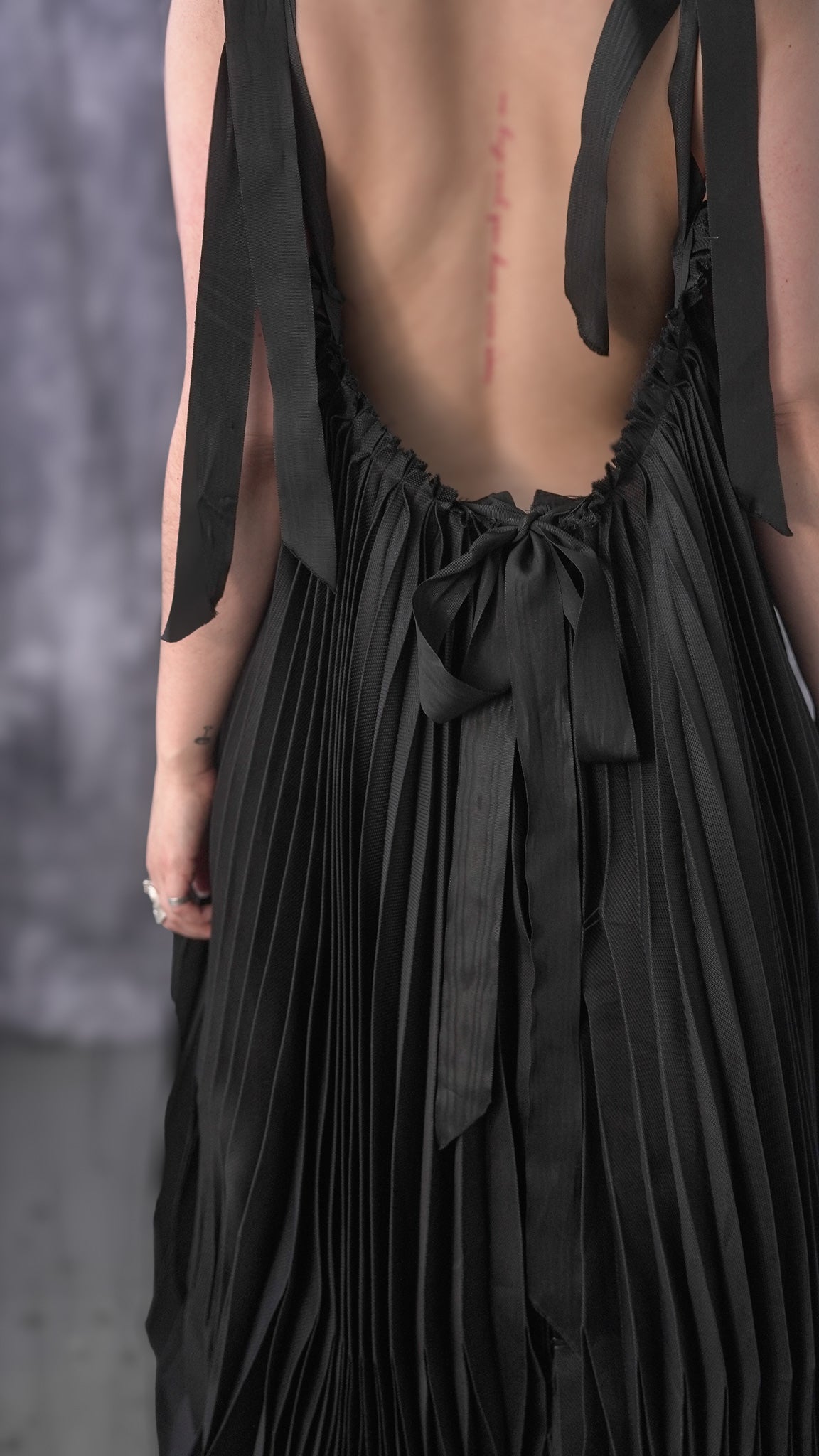 Black pleated silk gown dress with open back and ribbons on a blurred background