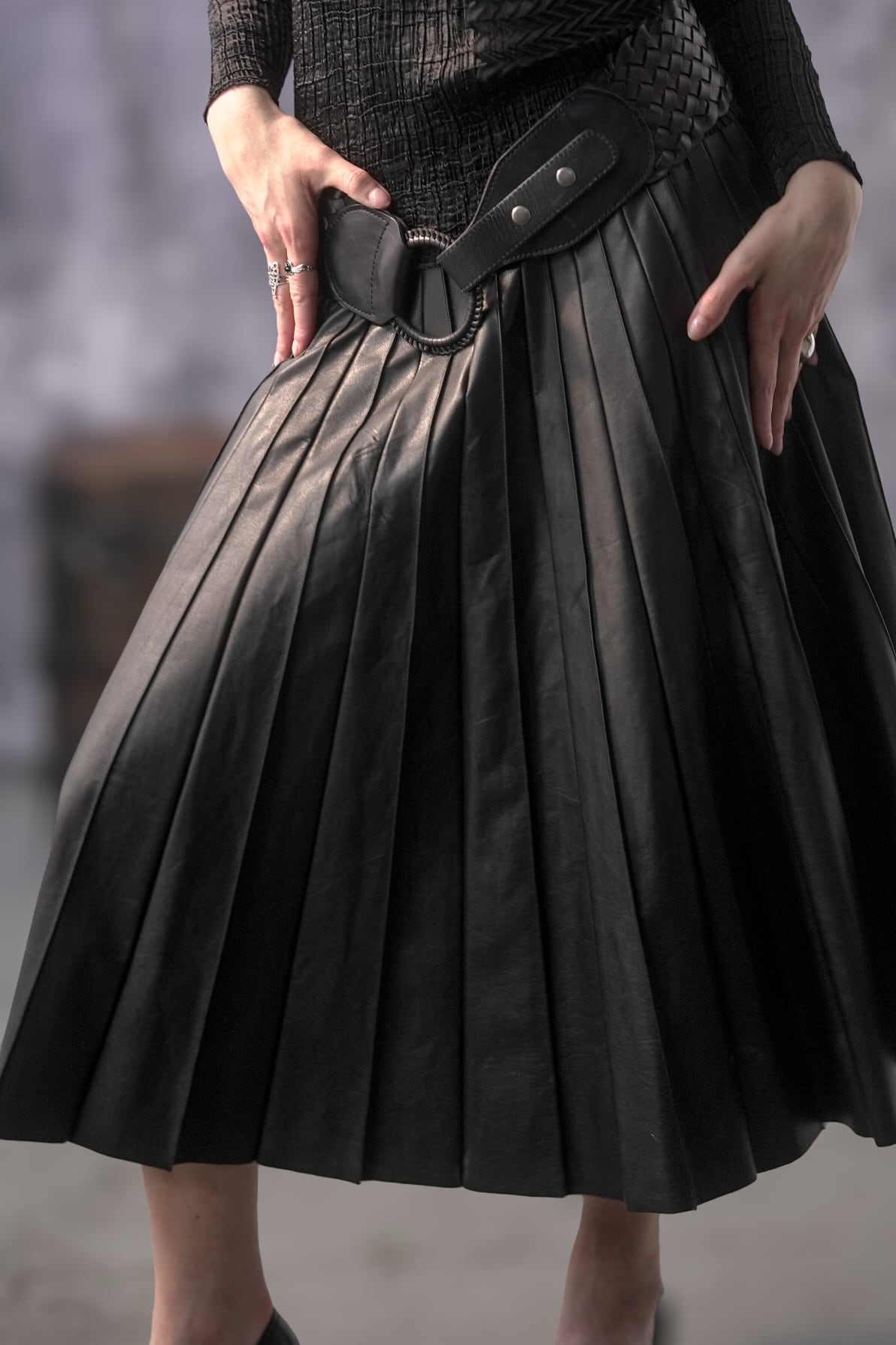 Black pleated skirt with a belt worn by a person, on a blurred background