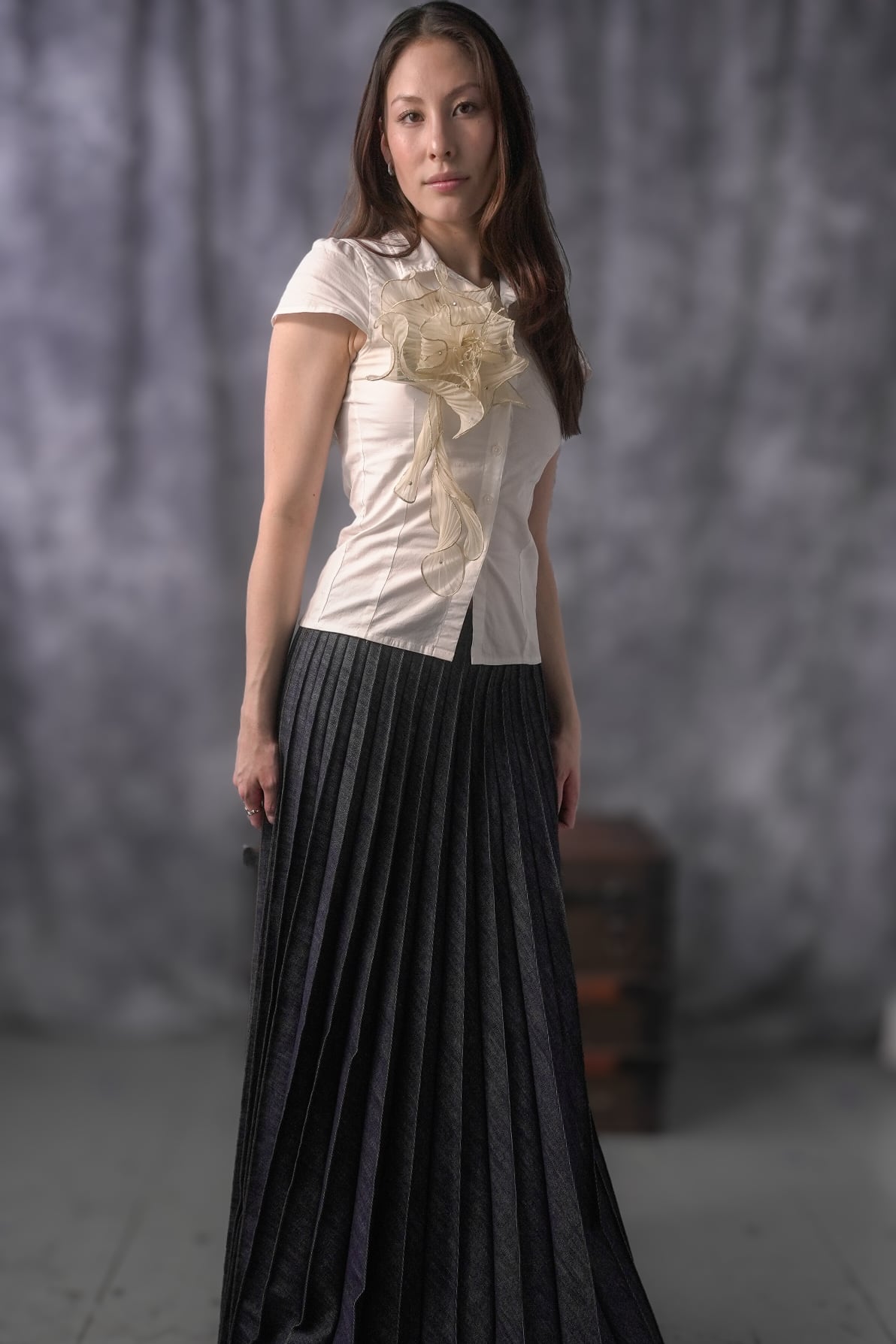 Woman wearing a white blouse with floral details and a black pleated skirt against a gray background