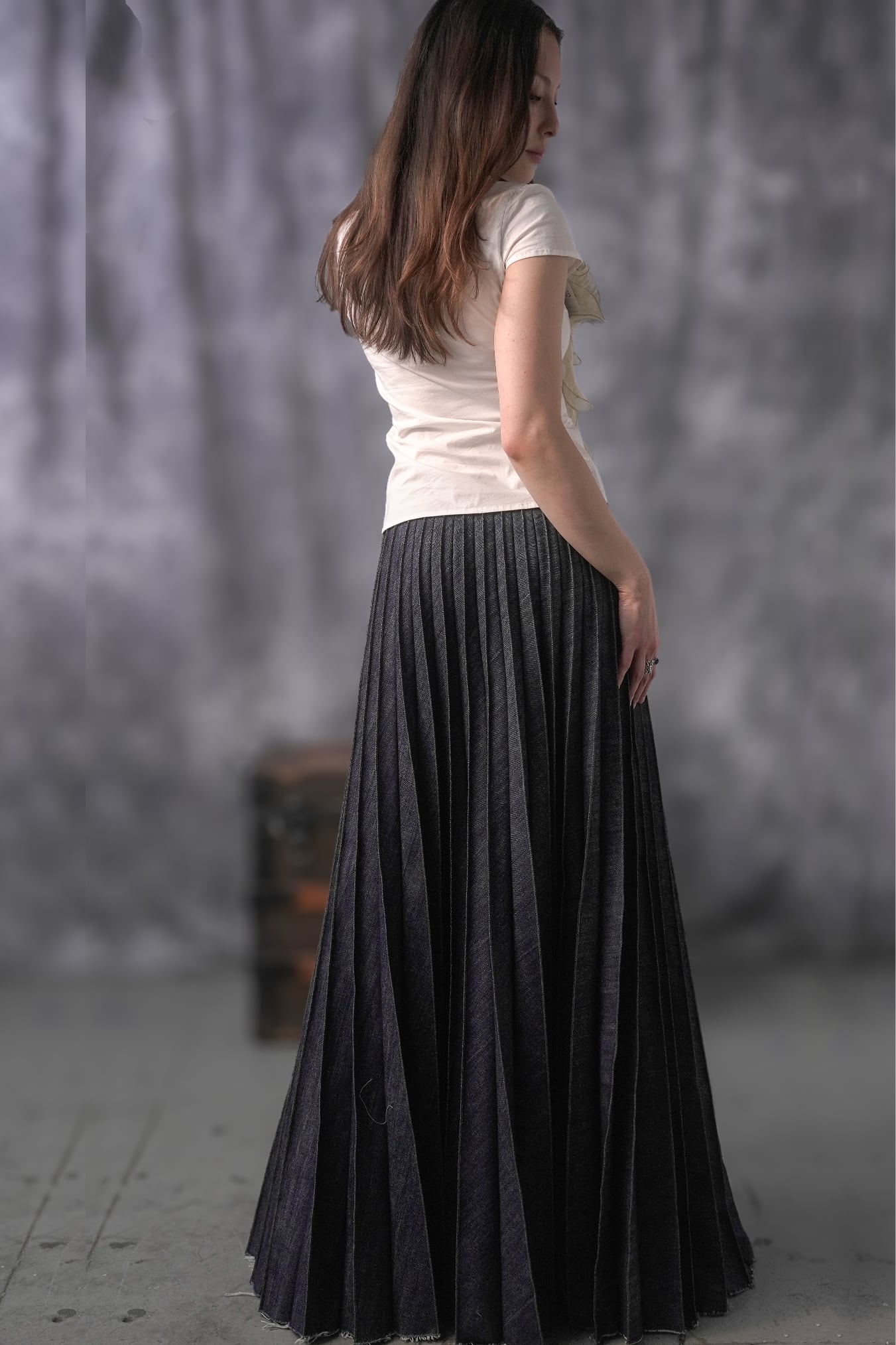 Woman wearing a white top and black pleated skirt against a gray background