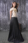 Woman wearing a white top with a large flower and a black pleated skirt against a gray background