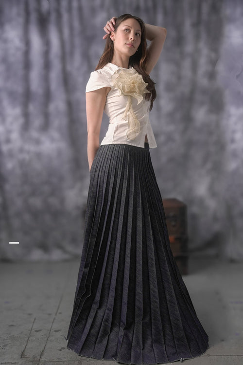 Woman wearing a white top with a large flower and a black pleated skirt against a gray background