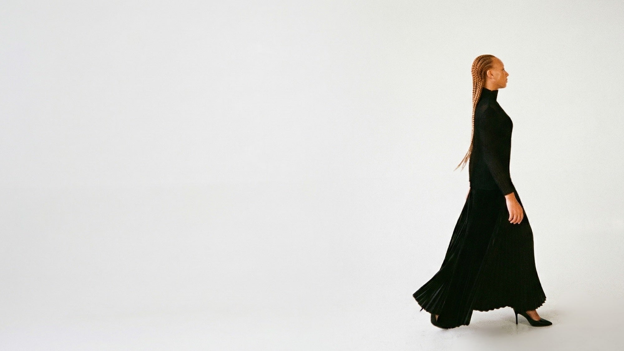 Woman walking in black charmeuse pleated pant. 
