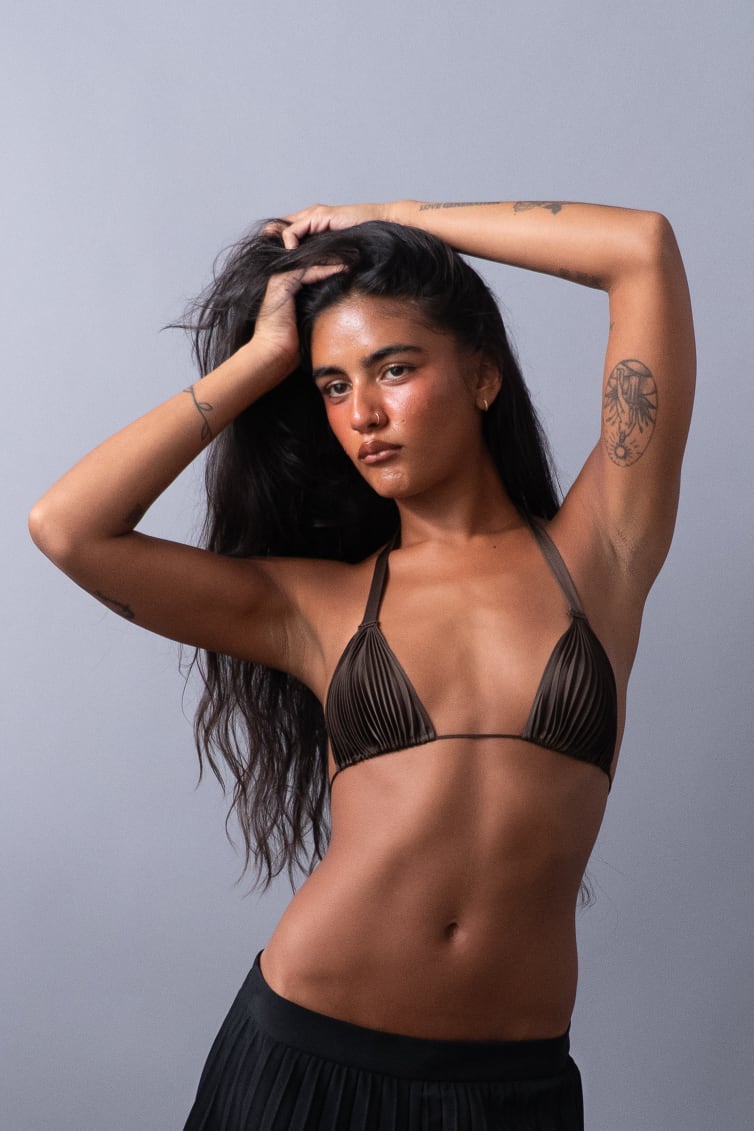 Female wearing a brown pleated bralette in a fashionable pose with pleated pants. 