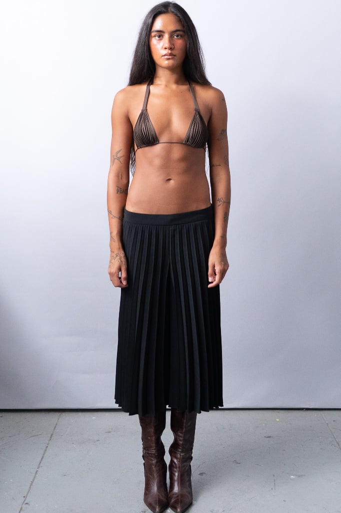 Full body shot of a girl wearing pleated capri pants and a pleated bralette. 